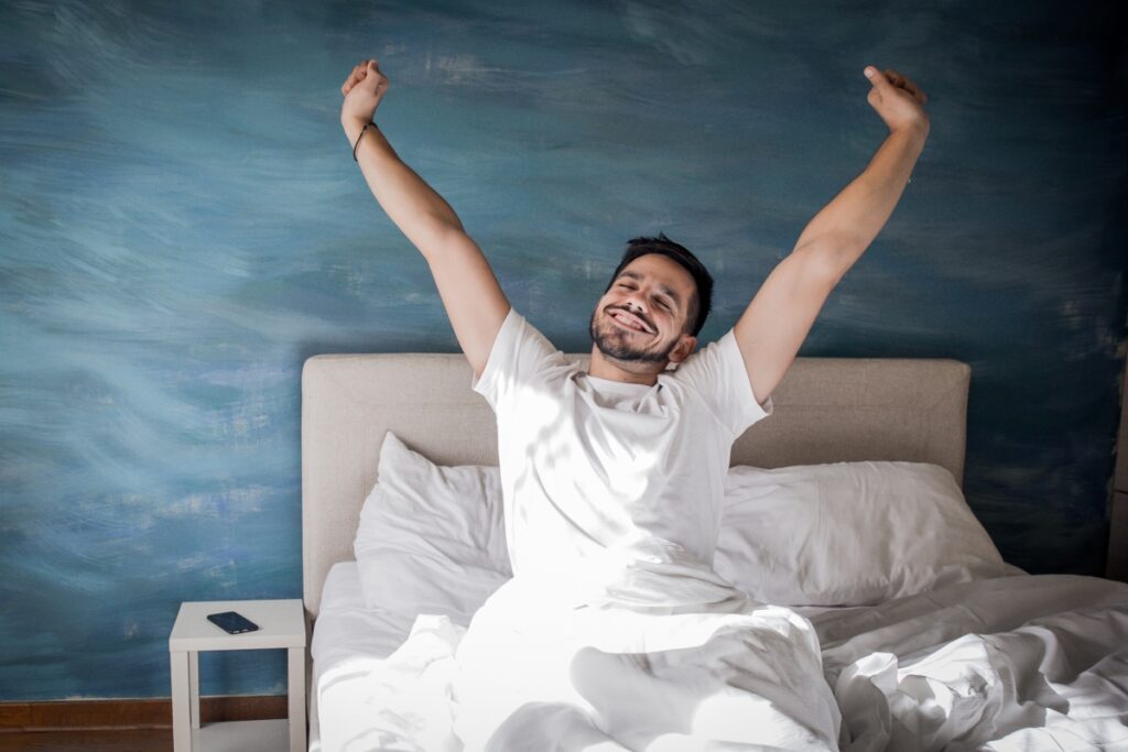 A happy man in a bed waking up and streaching his arms to the ceilling