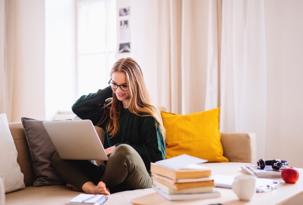 A young woman sitting in a couch stress free doing homework in her laptop