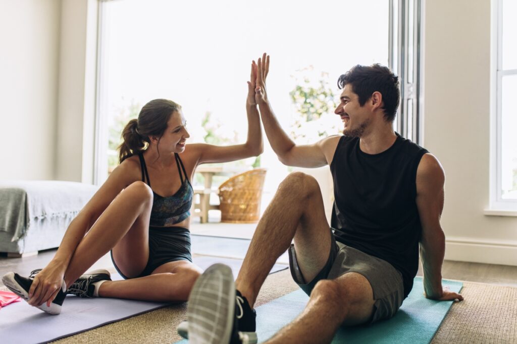 A couple sitting on the floor in their's yoga mat just finishing a workout and high-fiving proud 
