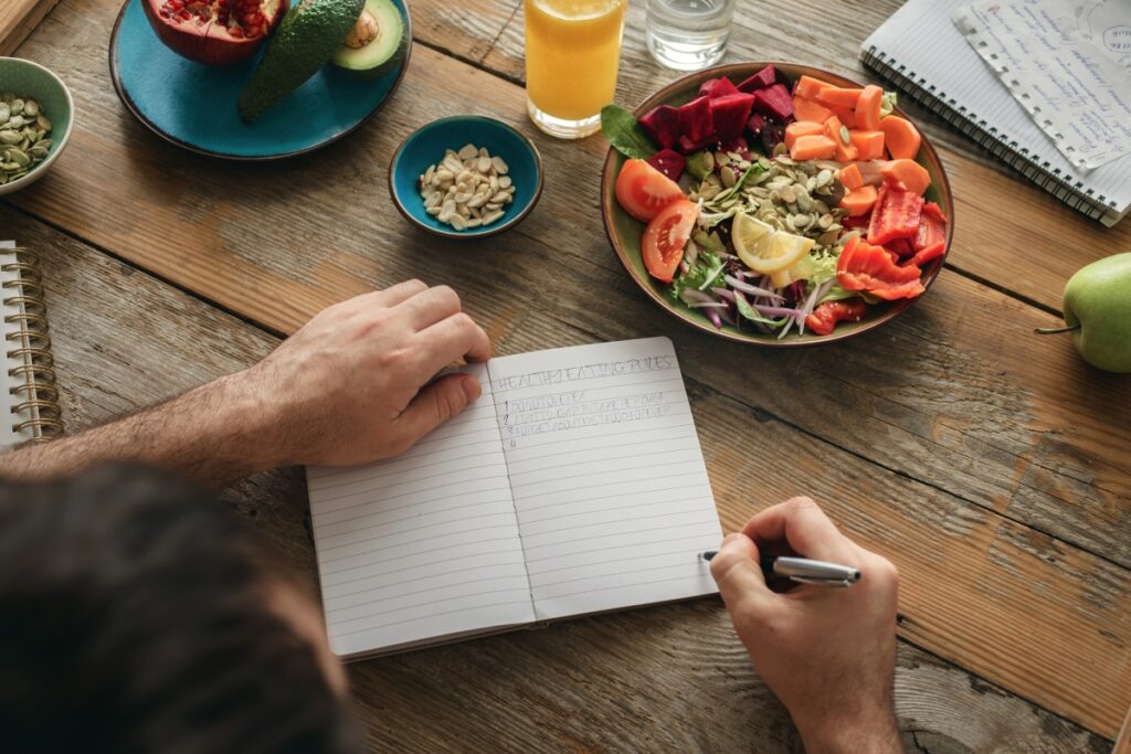 A person in a table writing Healthy eating habits in a notebook and a plate full with a salad