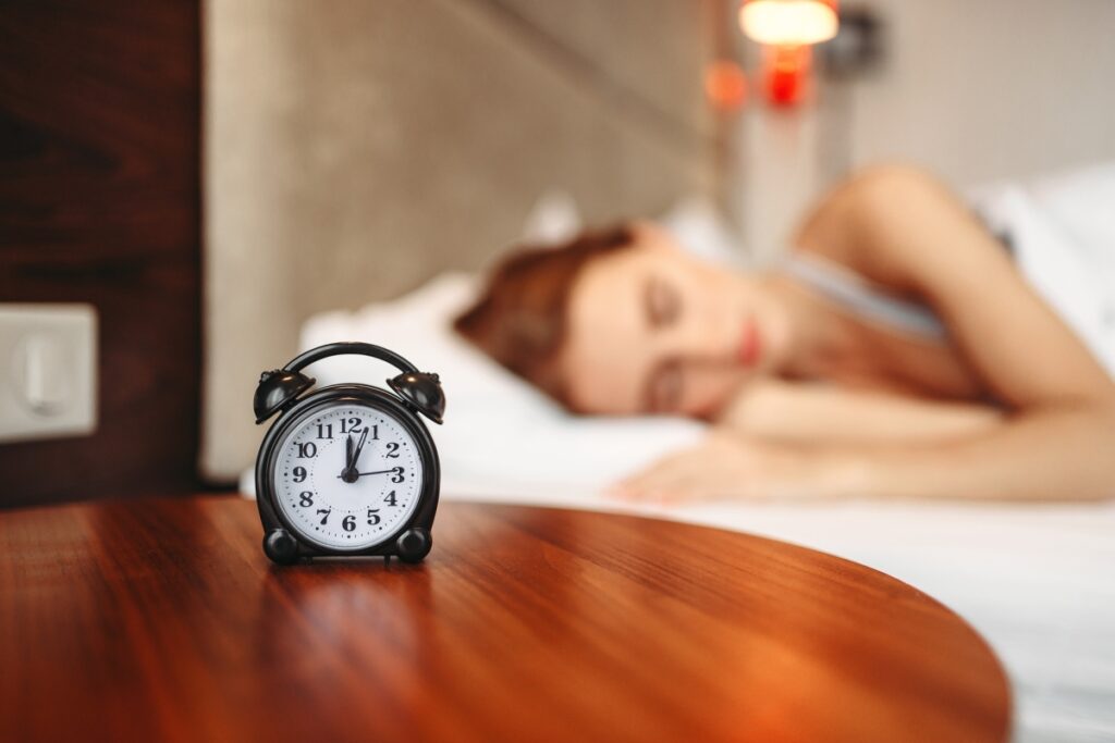 In the first plane is an alarm clock and in the background is a woman sleeping deeply