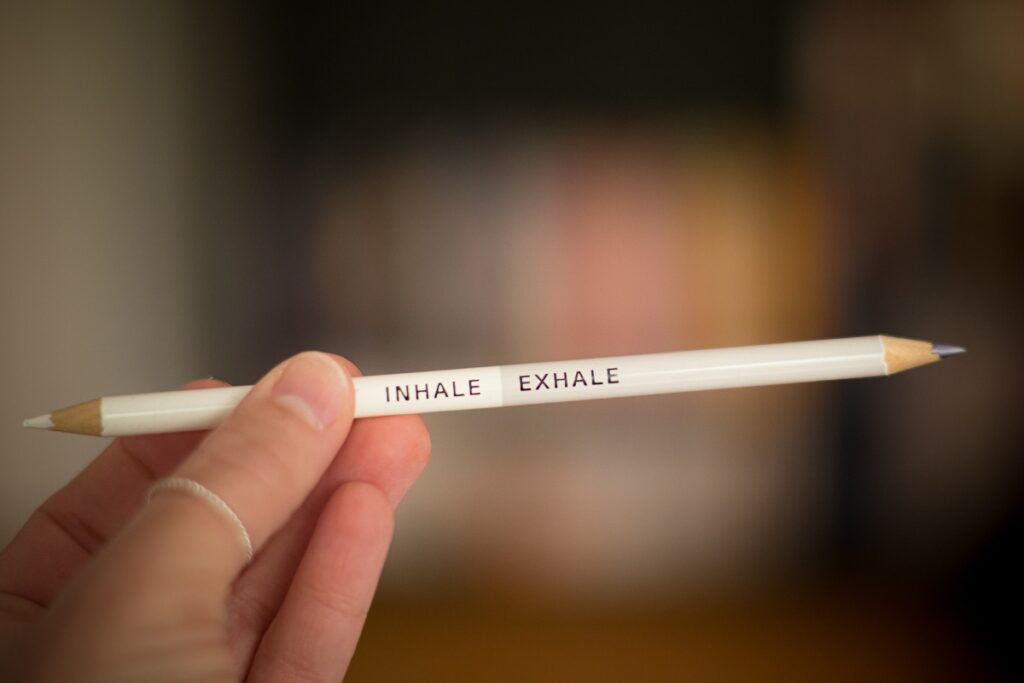 A hand holding a white pencil that has engraved the words inhale and exhale, and the background blurred
