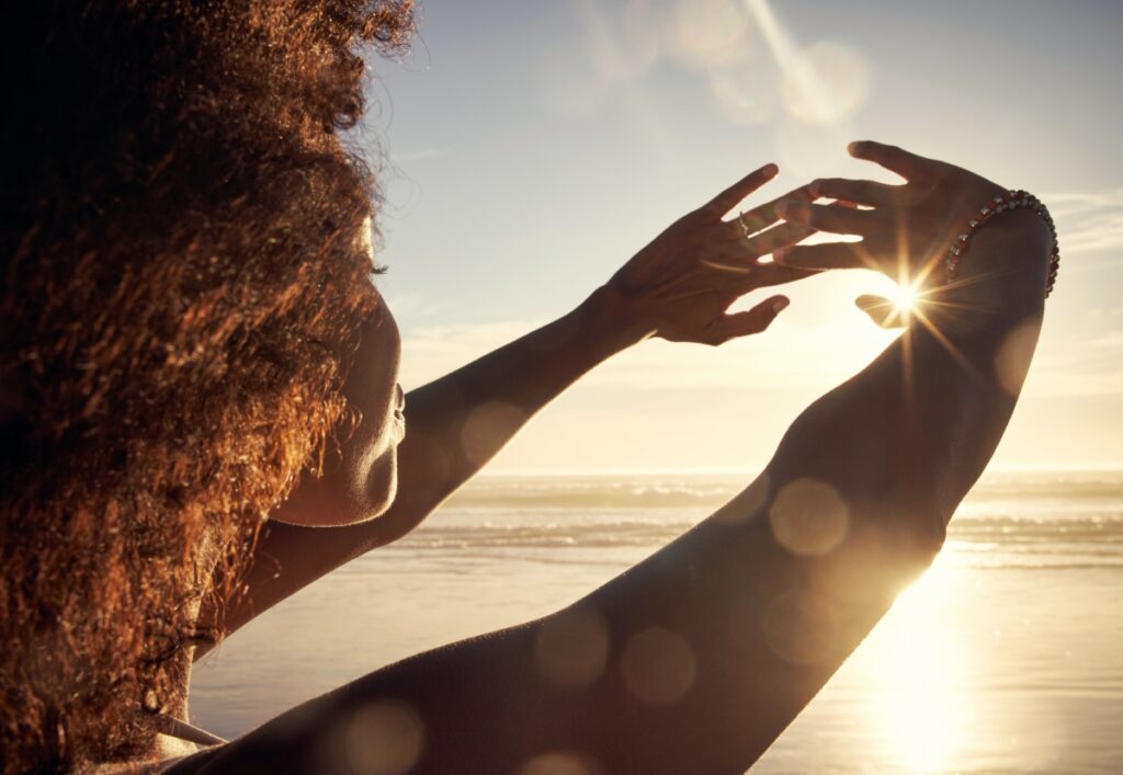 a woman in the sunset at the beach covering her eyes with her hands 