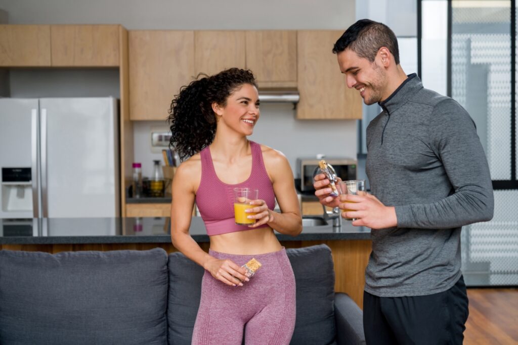 A man and a woman happy eating a protein bar and orange juice