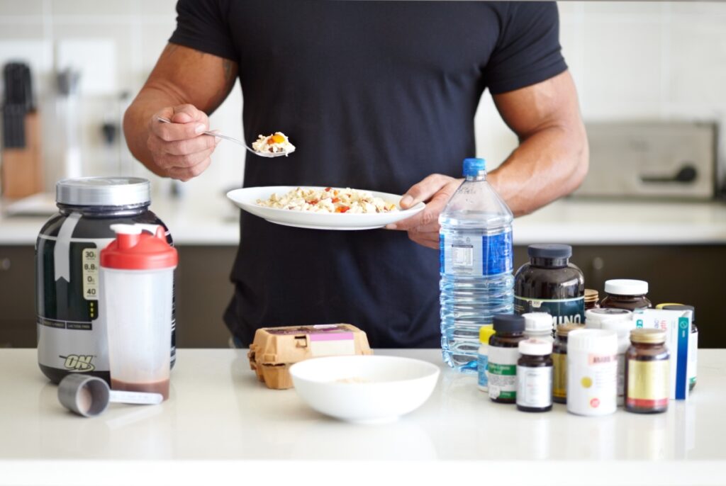 A person eating a meal and a table with protein powder, water, and supplements
