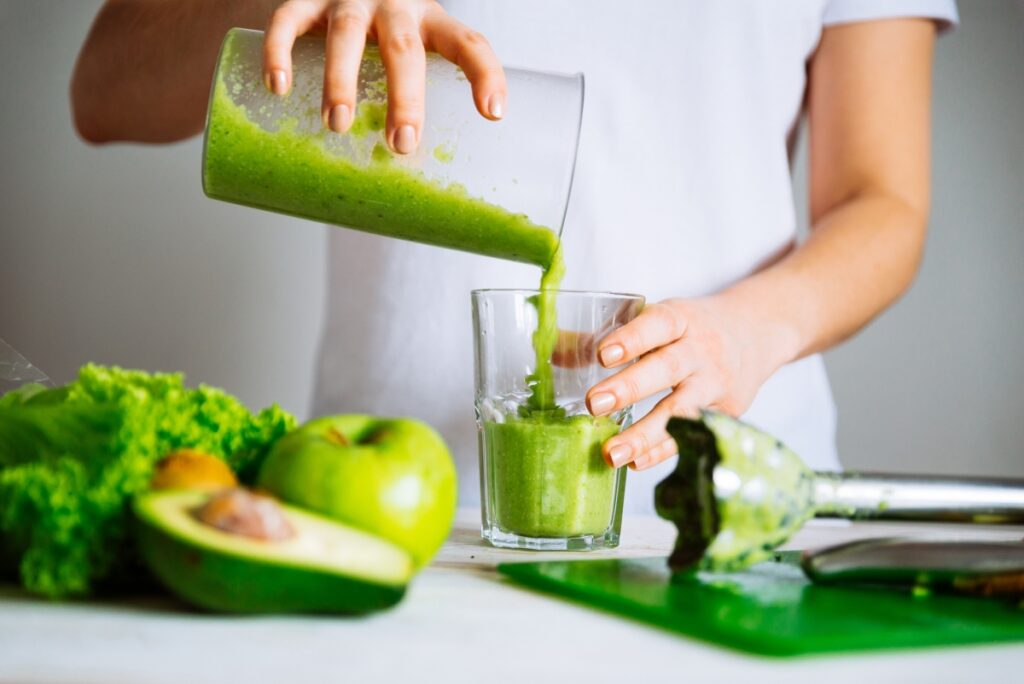 A person serving a green juice with apple, avocado, and fresh greens