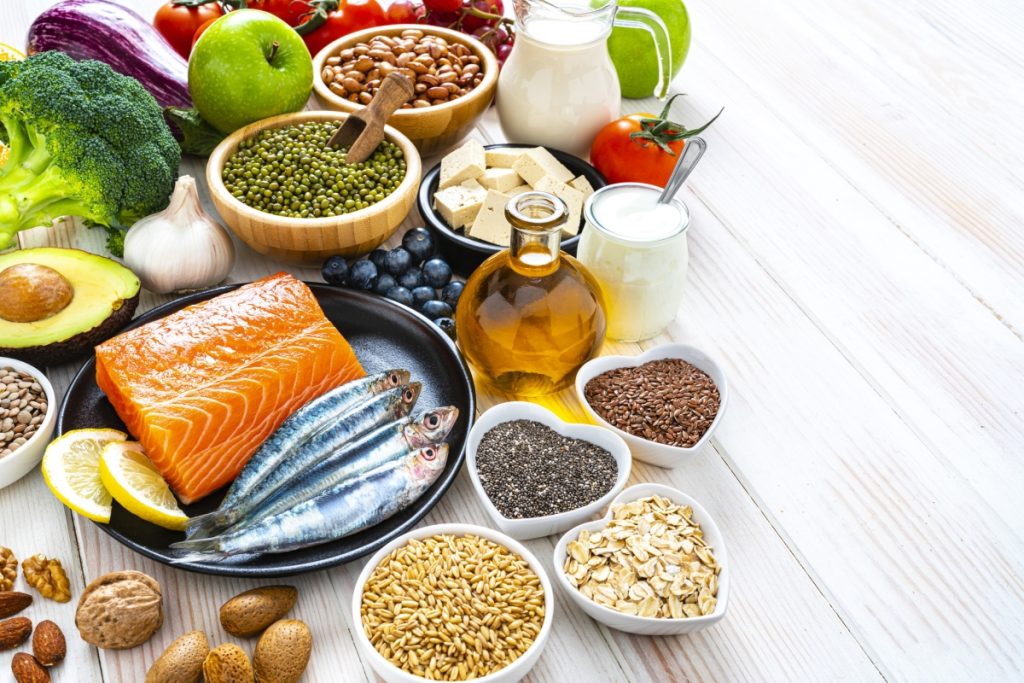 Healthy eating: group of fresh multicolored foods to help lower cholesterol levels shot on wooden table. The composition includes oily fish like salmon and sardines. Beans like Pinto beans and brown lentils.