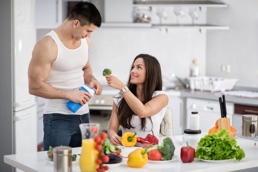 vegan bodybuilder next to his partner while she is oferring him broccoli