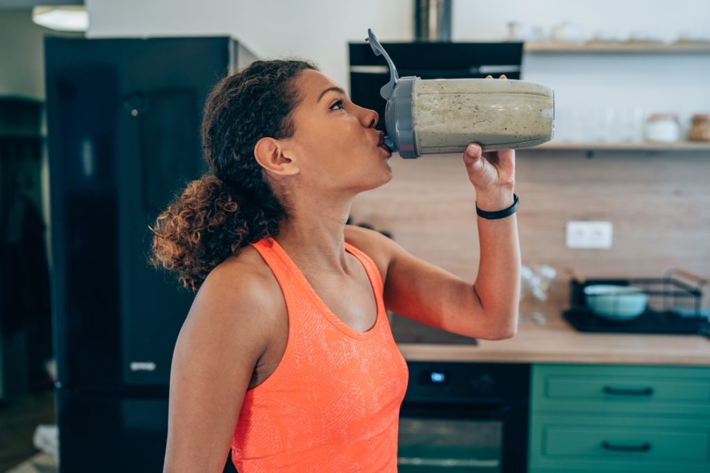Sportswoman drinking protein shake or smoothie after a home workout