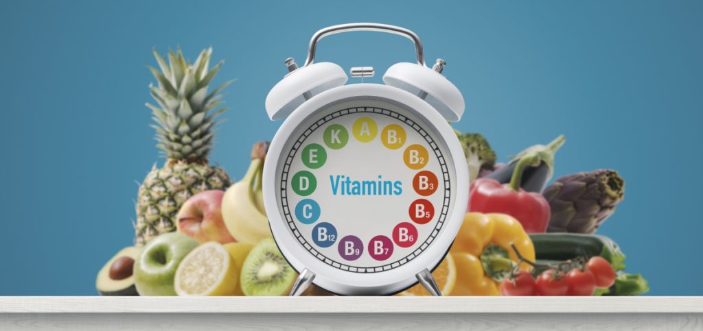 Alarm clock with b-complex, lots of vegetables and fruits in the background, healthy diet concept