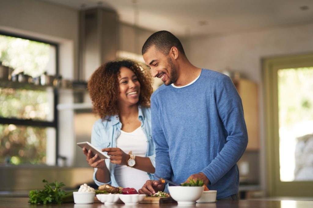 A happy young couple using a digital tablet while preparing a healthy meal together at home