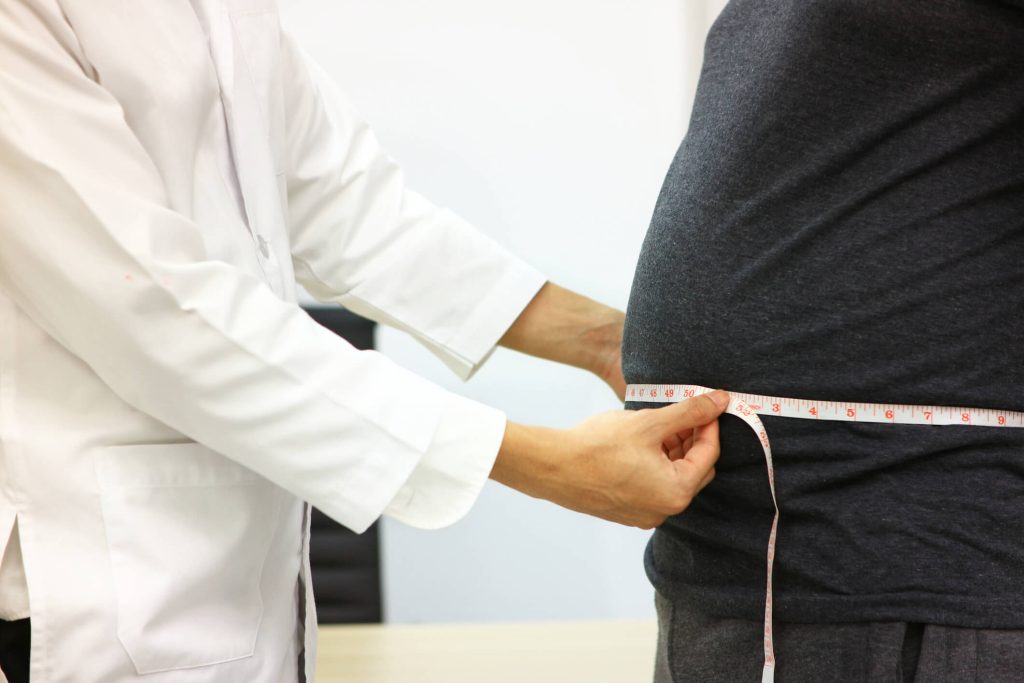 Doctor uses a tape measure to measure the waist of fat man