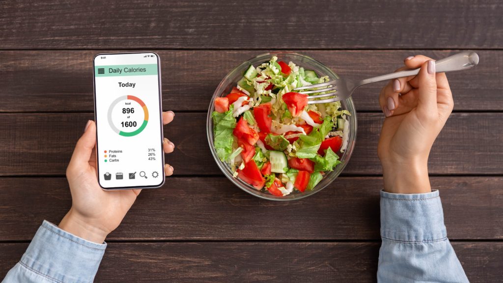 Smart eating and diet planning concept. Woman eating fresh vegetable salad and counting calories on Me diet app