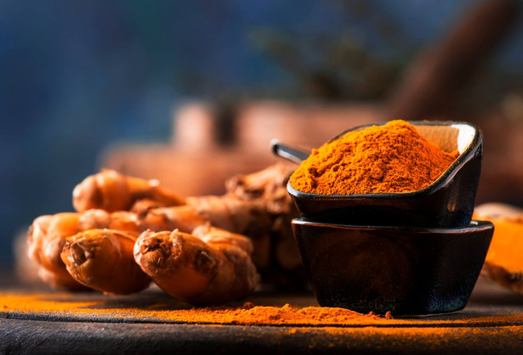 Turmeric powder and fresh turmeric on wooden background