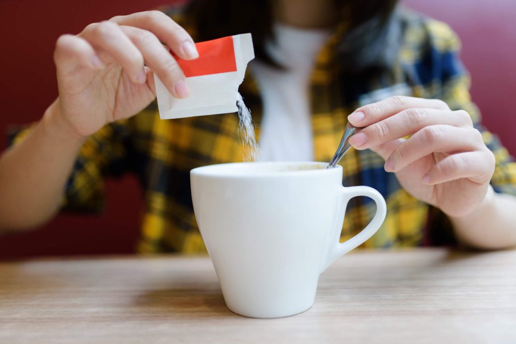 woman pouring sweetener into mug.