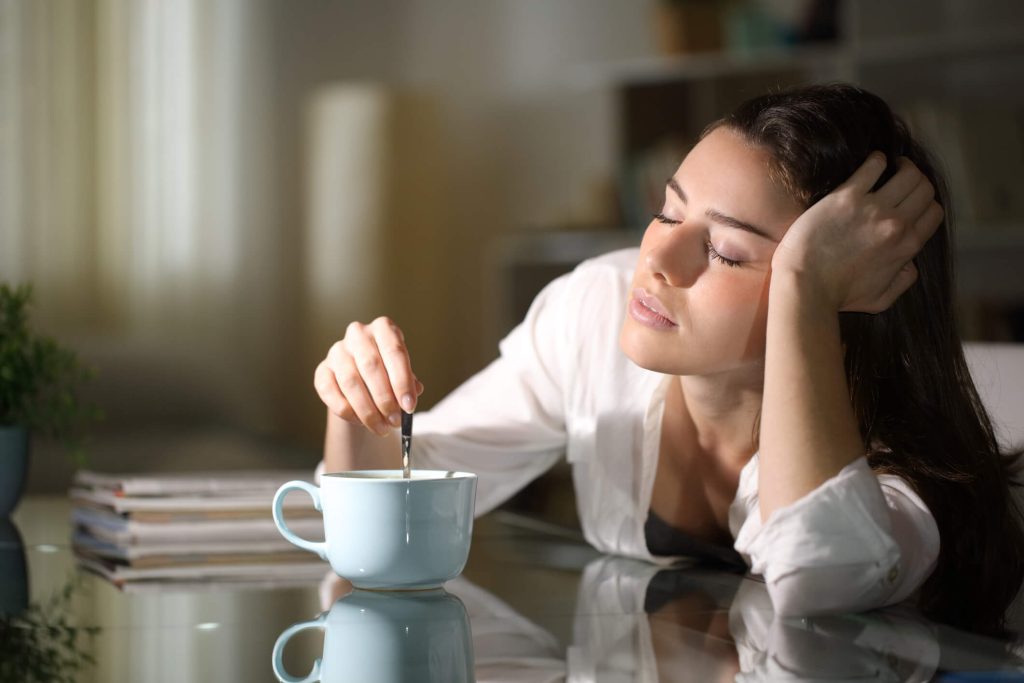 Sleepy woman stirring coffee in the morning