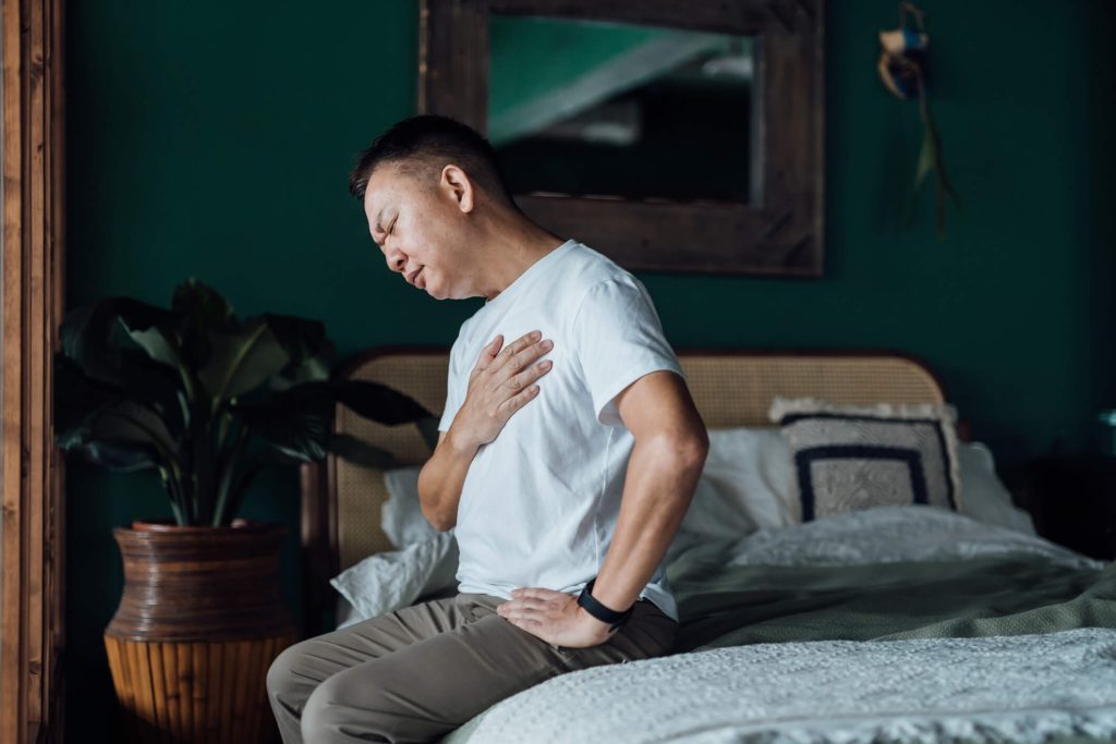 Senior Asian man with eyes closed holding his chest in discomfort, suffering from heart burn