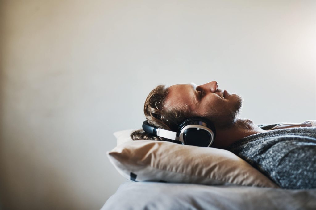 man sleeping with a headset listening to waves to improve sleep
