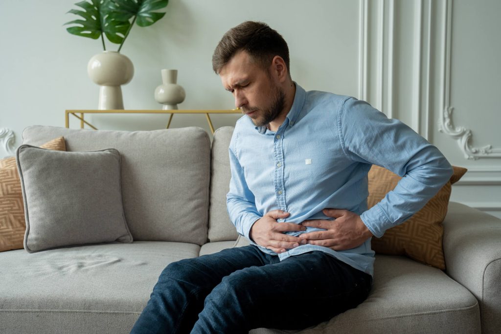 A man suffers from abdominal pain while sitting at home on the couch.