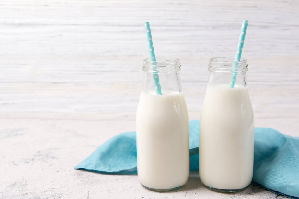 Two bottles of fresh milk with blue straws on wooden background