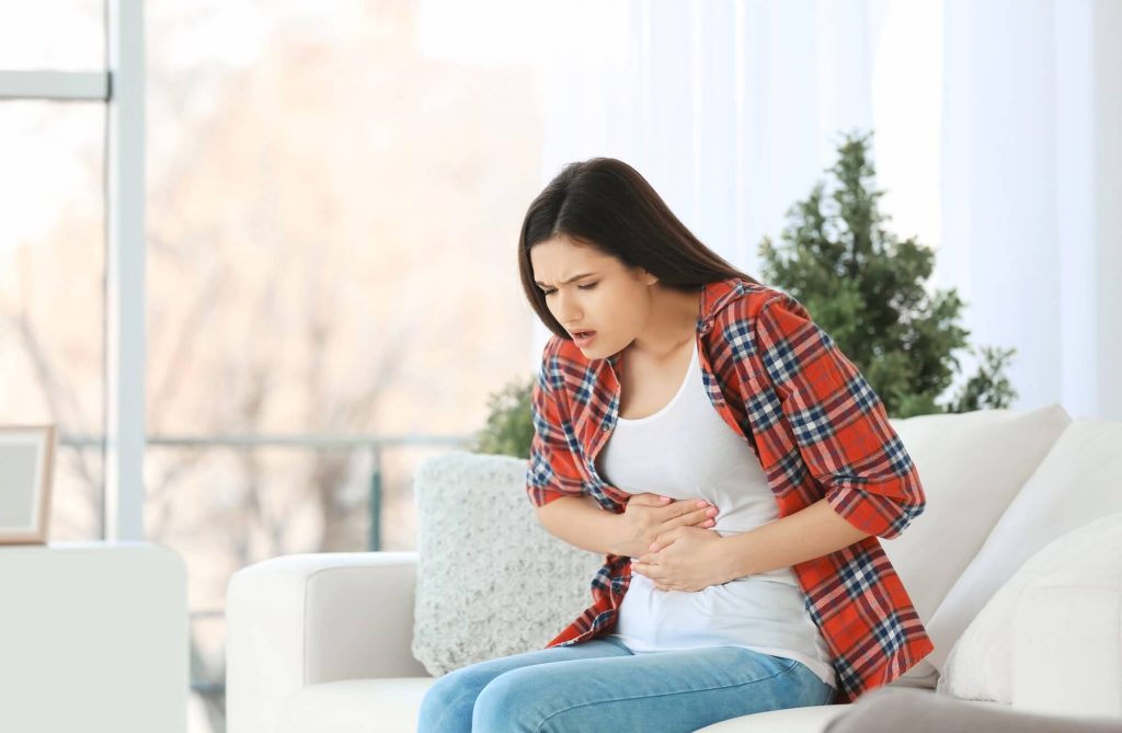 Woman sit down with hands over her hurting belly