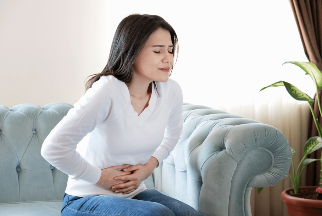 woman sitting in a couch with stomach ache, hands over her belly