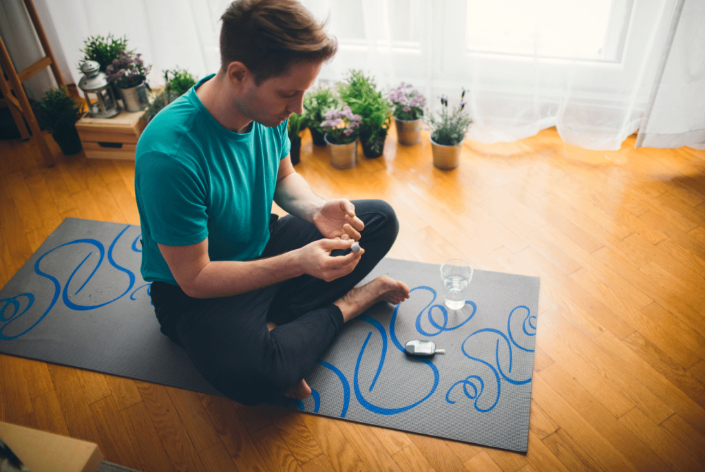 man sitting on a mat checking his blood sugar 