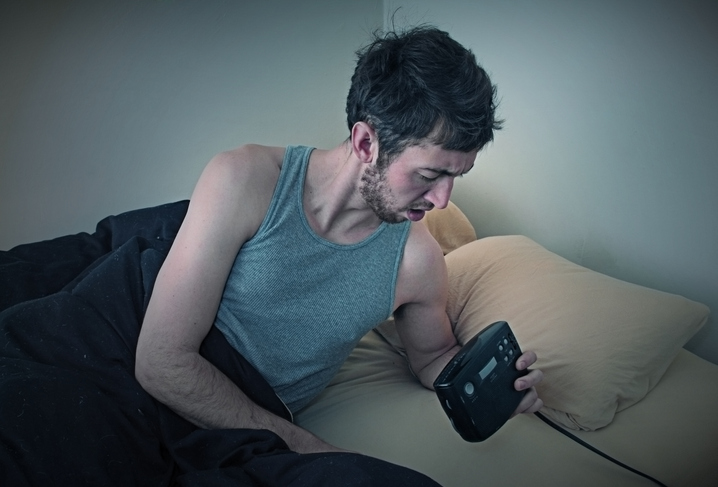 A young adult having trouble sleeping looks at the time in his bedroom.