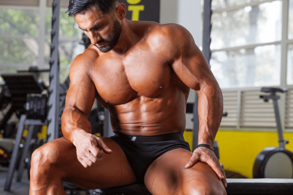 male bodybuilder shirtless sitting on a bench looking sad