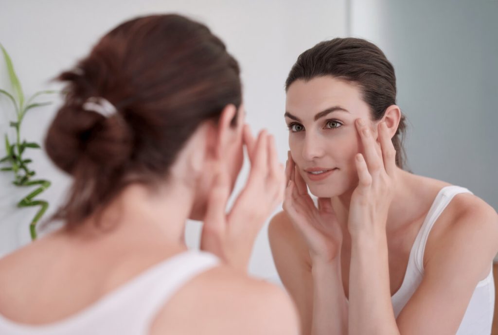 beautiful woman looking her skin on a mirror