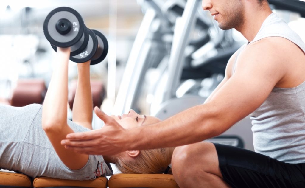 personal trainer teaching a woman to do a dumbbell chest press 