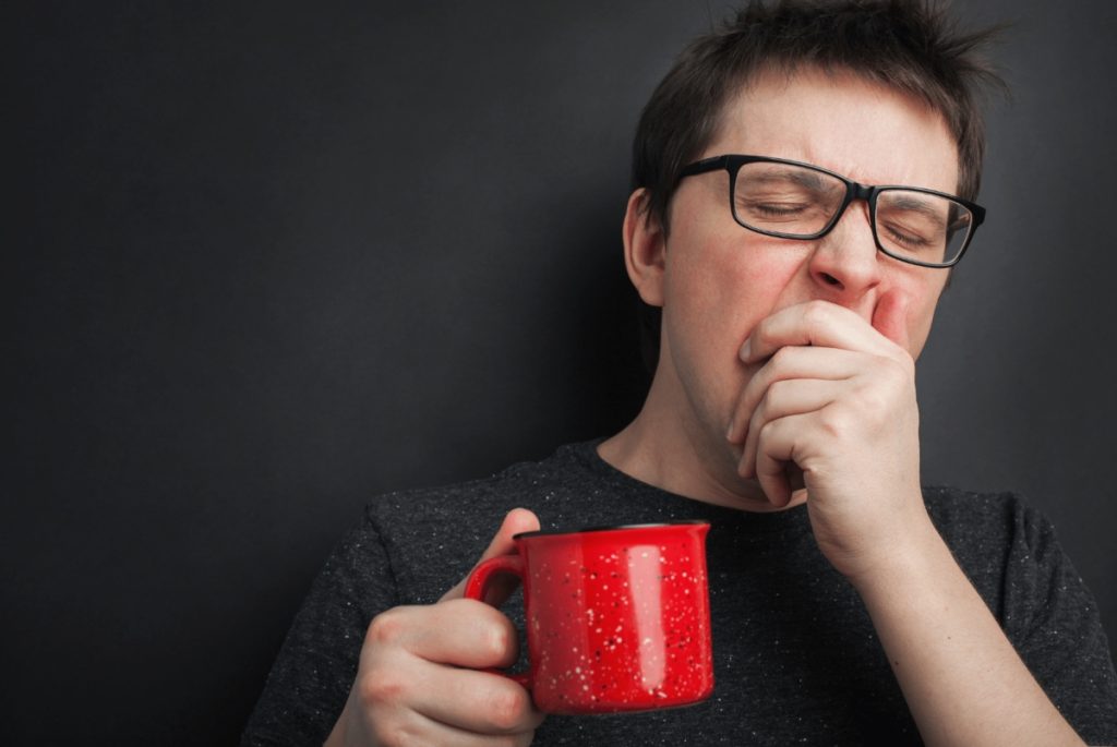 Man Yawning with a red cup of coffee