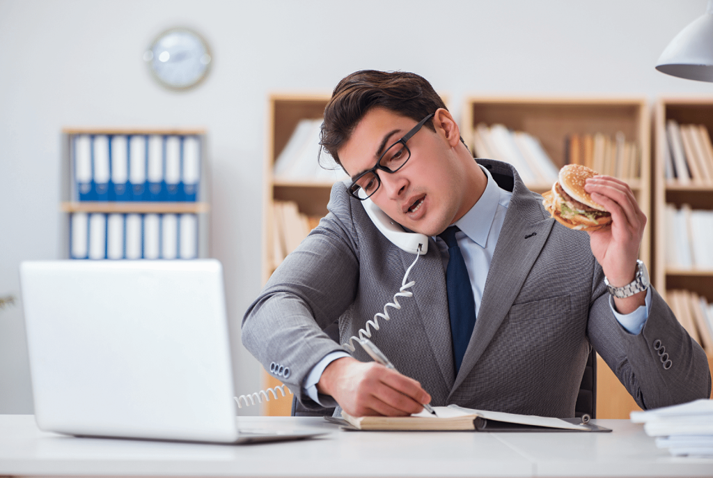 man eating a burger while answering the phone and taking notes at work 