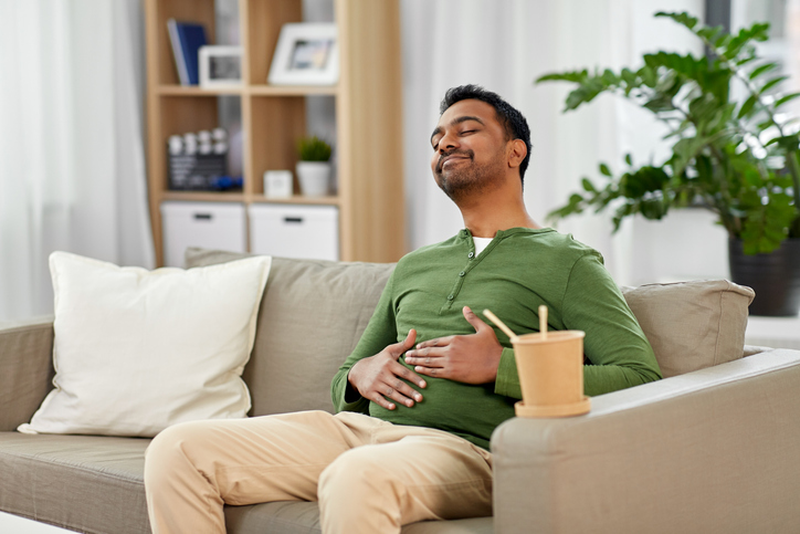 consumption and people concept - full and pleased indian man eating takeaway food at home