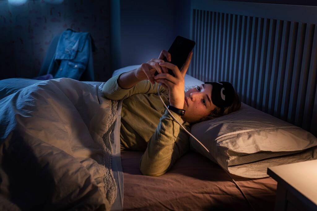 young woman checking phone in bed at night