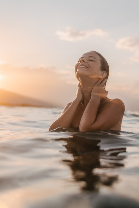 A young woman in the sea water enjoying the sea and the sunset under mountain Olympus