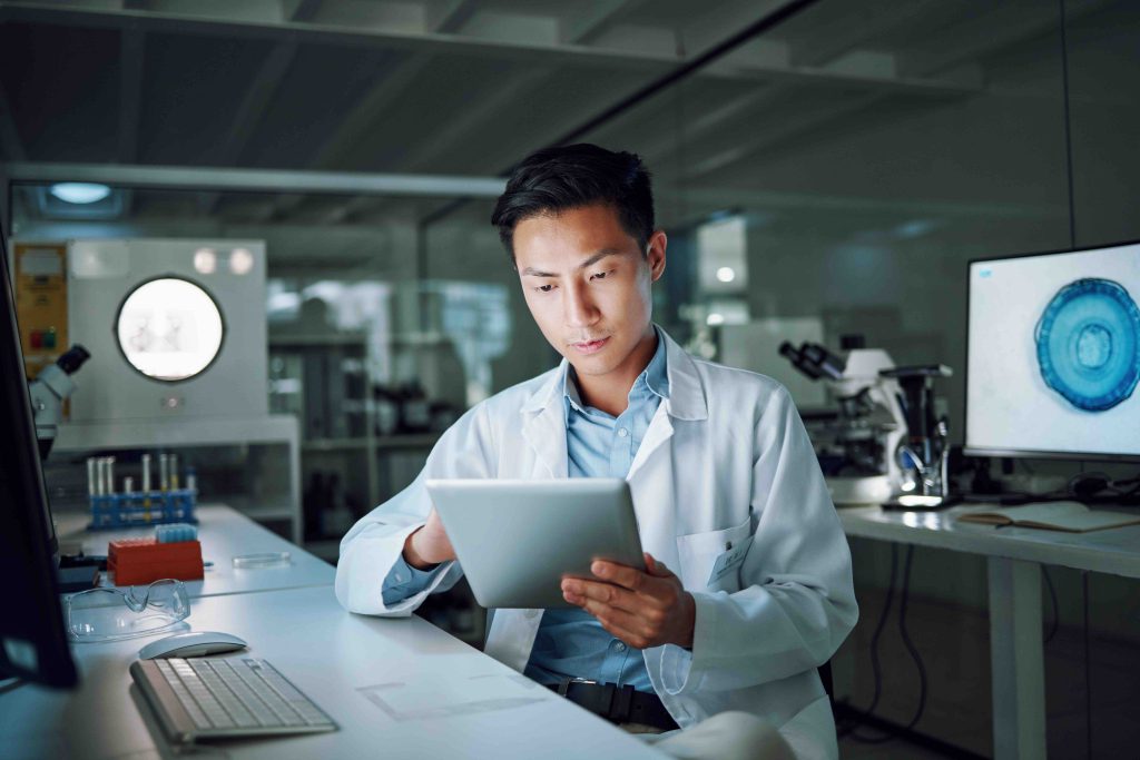 Tablet, planning and scientist with digital innovation, data and reading in laboratory. Asian man, doctor and information technology for futuristic medical research with pharma healthcare study