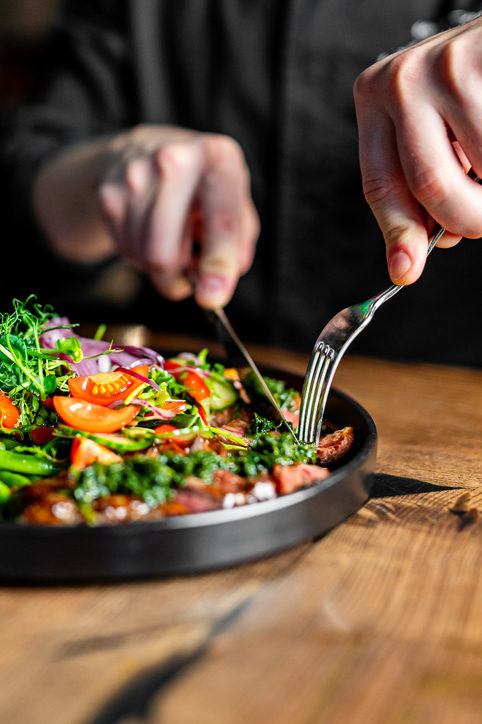 Hands of a man with a fork and knife eating a salad