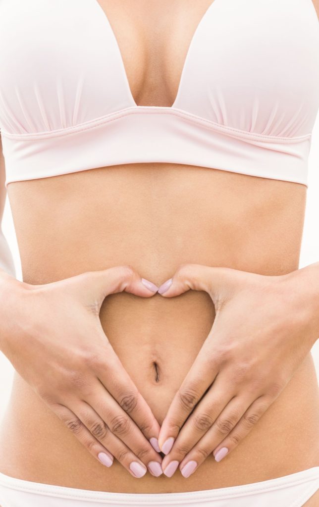 Woman with her hand in the shape of her heart around her belly button. 