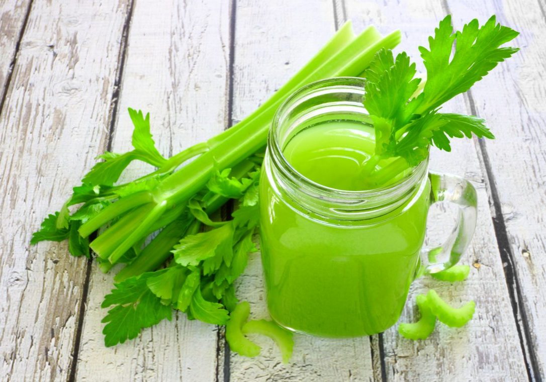 Celery juice in a mason jar glass. Downward view over a rustic white wood background.