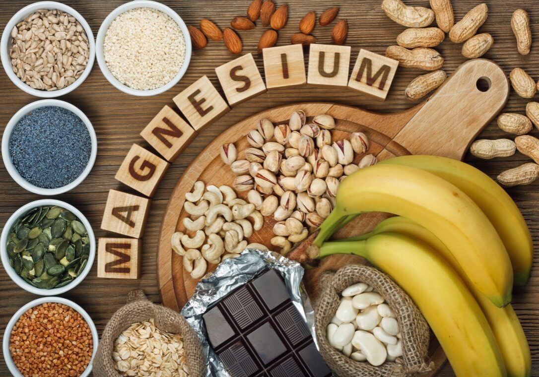Products containing magnesium: bananas, pumpkin seeds, blue poppy seed, cashew nuts, beans, almonds, sunflower seeds, oatmeal, buckwheat, peanuts, pistachios, dark chocolate and sesame seeds on wooden table