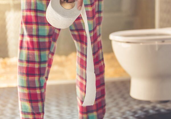 Cropped image of beautiful young woman in pajama holding a toilet paper while going to the toilet