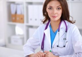 Beautiful young smiling female doctor sitting at the desk and writing.