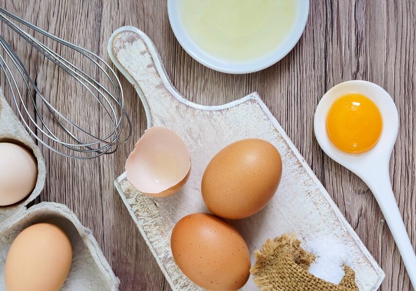 Fresh farm eggs on a wooden rustic background. Separated egg white and yolks, broken egg shells. Whipping eggs with whisk. Preparation of food from chicken eggs. The top view. View from above.
