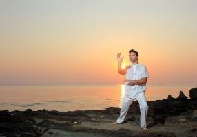 Handsome man practicing thai chi on the beach at sunrise