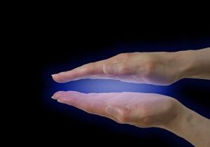 Female parallel hands demonstrating the blue electromagnetic healing energy that can be seen by those who see auras, on a black background