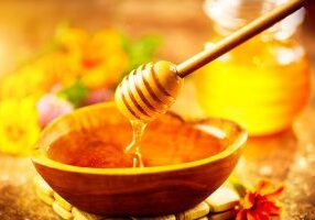 Honey dripping from honey dipper in wooden bowl.  Close-up. Healthy organic Thick honey pouring from the wooden honey spoon, closeup. Sweet dessert background