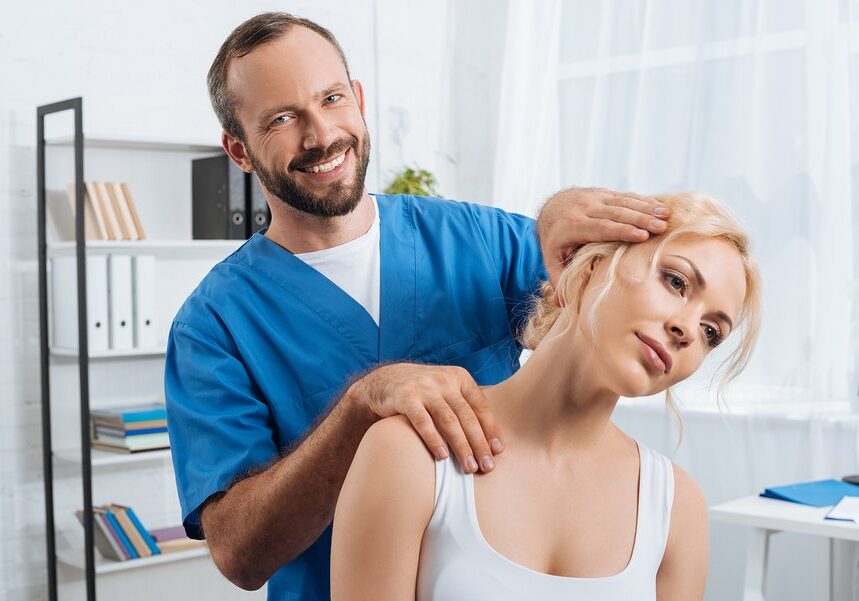 portrait of smiling chiropractor stretching neck of woman during appointment in hospital